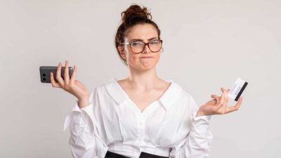 A puzzled female investor shrugging with credit card and phone.