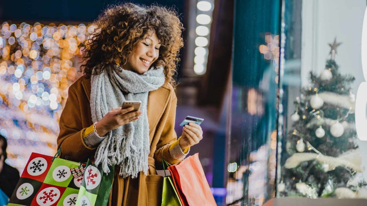A woman Christmas shopping while holding bags and a credit card.