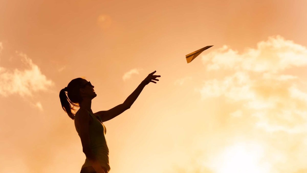 A woman sends a paper plane soaring into the sky at dusk.