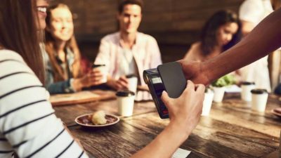A diner uses her phone to pay for the bill at a restaurant as she sit at a table with three other having finished a meal together.