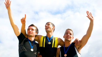 three men stand on a winner's podium with medals around their necks with their hands raised in triumph.