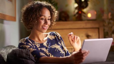 A smiling woman looks at her computer laptop in her home with warm lights in the background feeling happy to see the EMvision share price rising