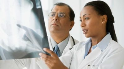 Two doctors wearing white coats look closely at a medical imaging x-ray as the share prices of ASX 200 healthcare shares improve in FY23