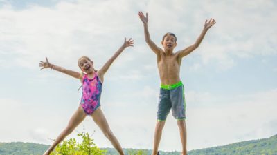 Two kids do big star jumps into the pool.