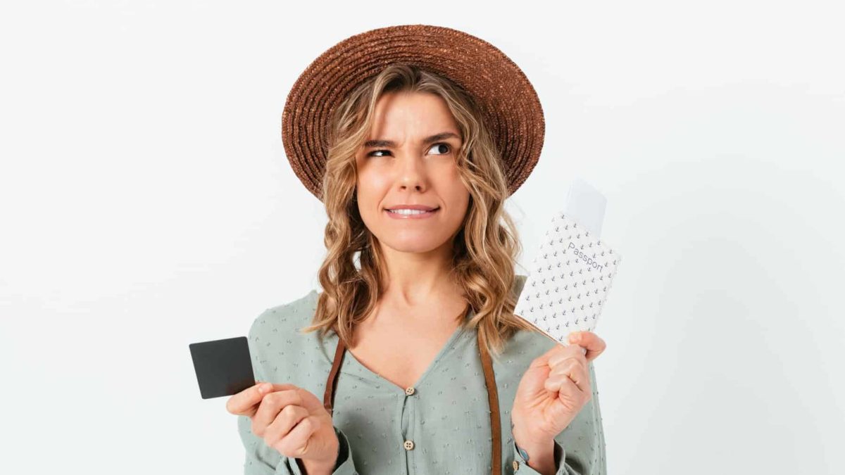 A girl holds a ticket and a passport in either hand and has a confused, vexed look on her face as though she is unsure.