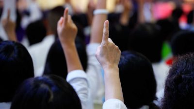 Two bidders raise their hands in the air to bid up the price of an ASX 200 share