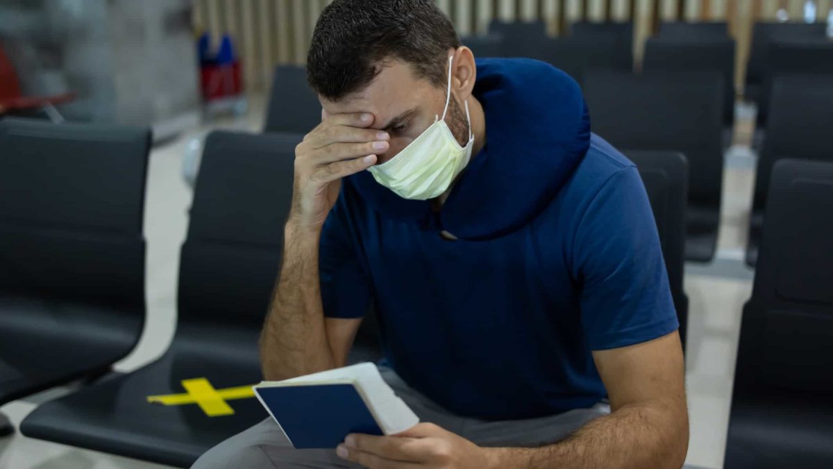 pset man traveler with a medical mask on face sitting in airport or train station after delayed, missed or canceled departure.