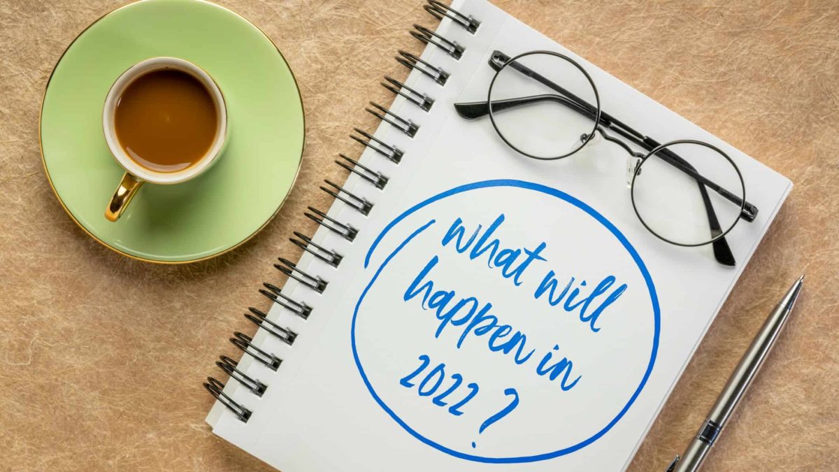 A notebook saying 'what will happen in 2022', with glasses and a mug of coffee.
