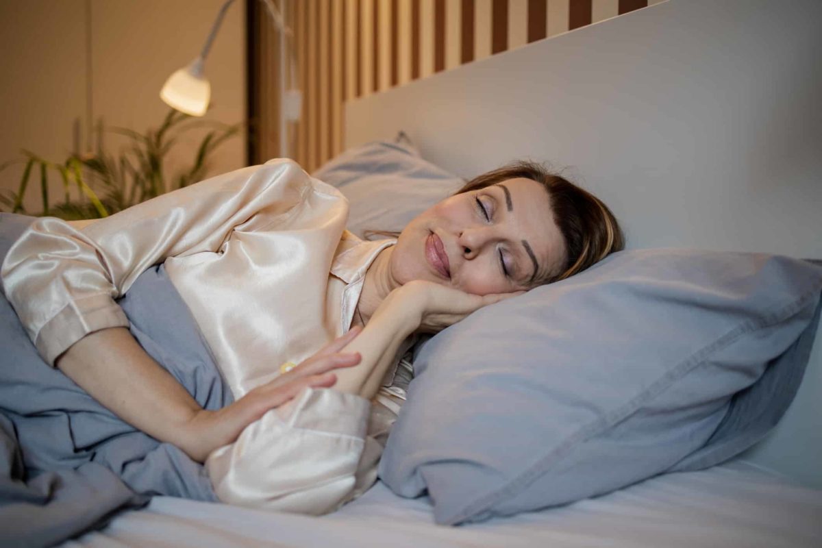 a mature woman sleeps peacefully in bed with a smile on her face as though she is very satisfied about something.
