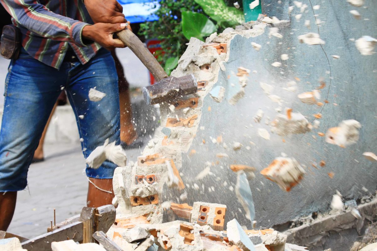 A person smashes a wall with a hammer, sending bricks flying.