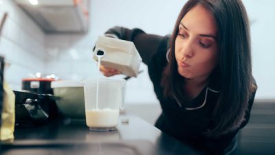 A woman is unsure as she pours milk into a glass, has it gone sour?