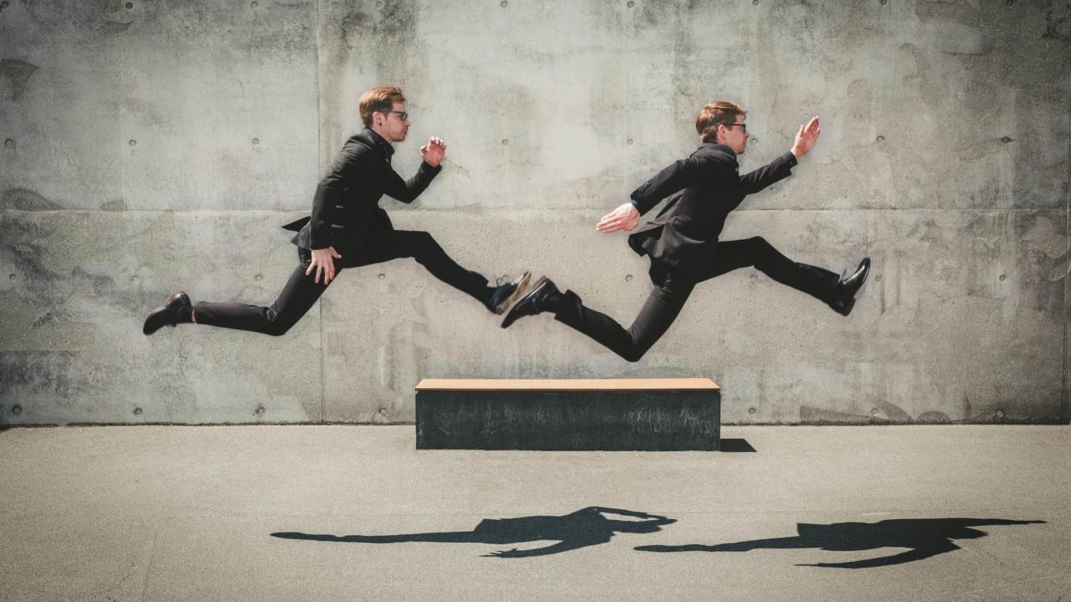 Two businesspeople in suits run, one chasing the other.