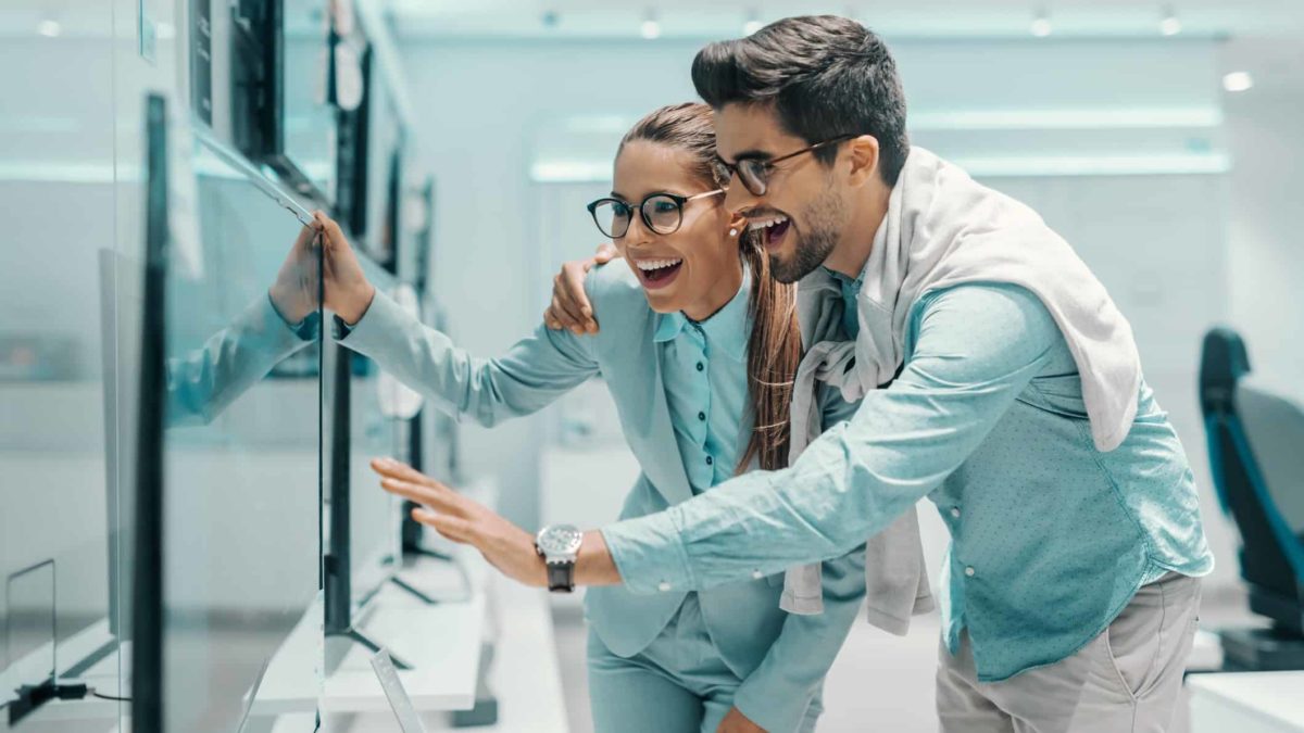 A couple look excited while buying a television in a tech store.