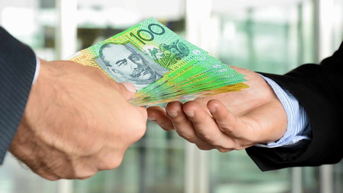 Close-up photo of a human hand with $100 bills offering the money to another human hand