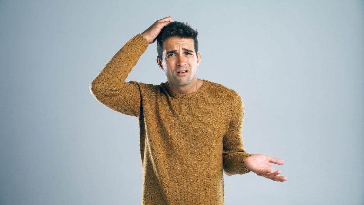A young man stands facing the camera and scratching his head with the other hand held upwards wondering if he should buy Whitehaven Coal shares