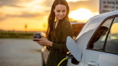 A woman smiles as she powers up her electric car using a fast charger.