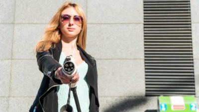 a woman holds out an electric vehicle charger with a satisfied look on her face behind cool sunglasses.