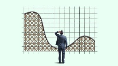 A man in a business suit scratches his head looking at a graph that started high then dips, then starts to go up again like a rollercoaster.