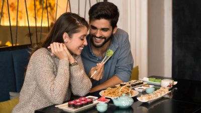 A man and woman sit closely together in a restaurant eating sushiA couple sits together