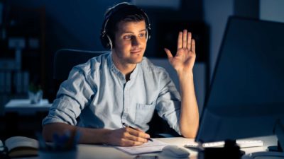 Man waves goodbye while looking at computer sitting at desk.