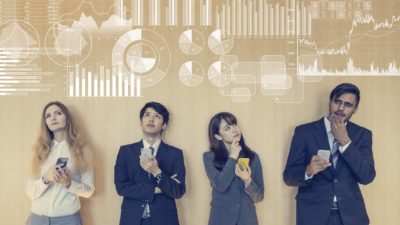 A group of people in business attire stand in a line against a wall, each with considered expressions on their faces, and superimposed above them a montage of graphs, charts, figures and metrics.