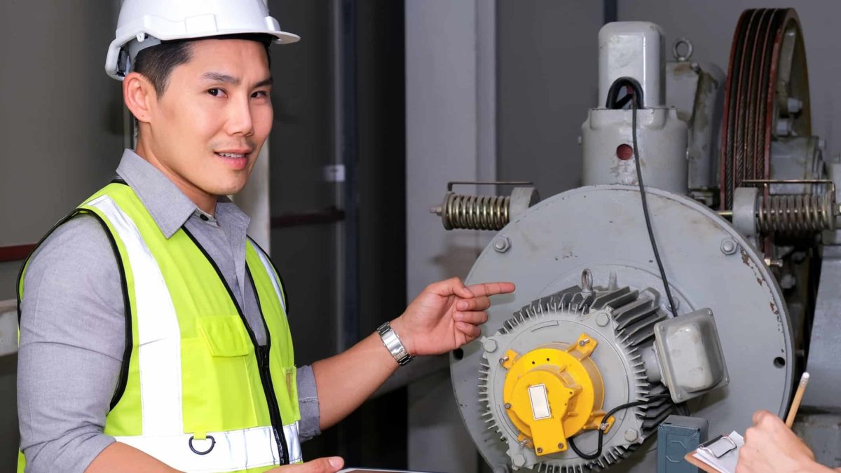a man in a hardhat inspects equipment in a processing plant looking towards the camera with a small smile with his hand on the machinery.