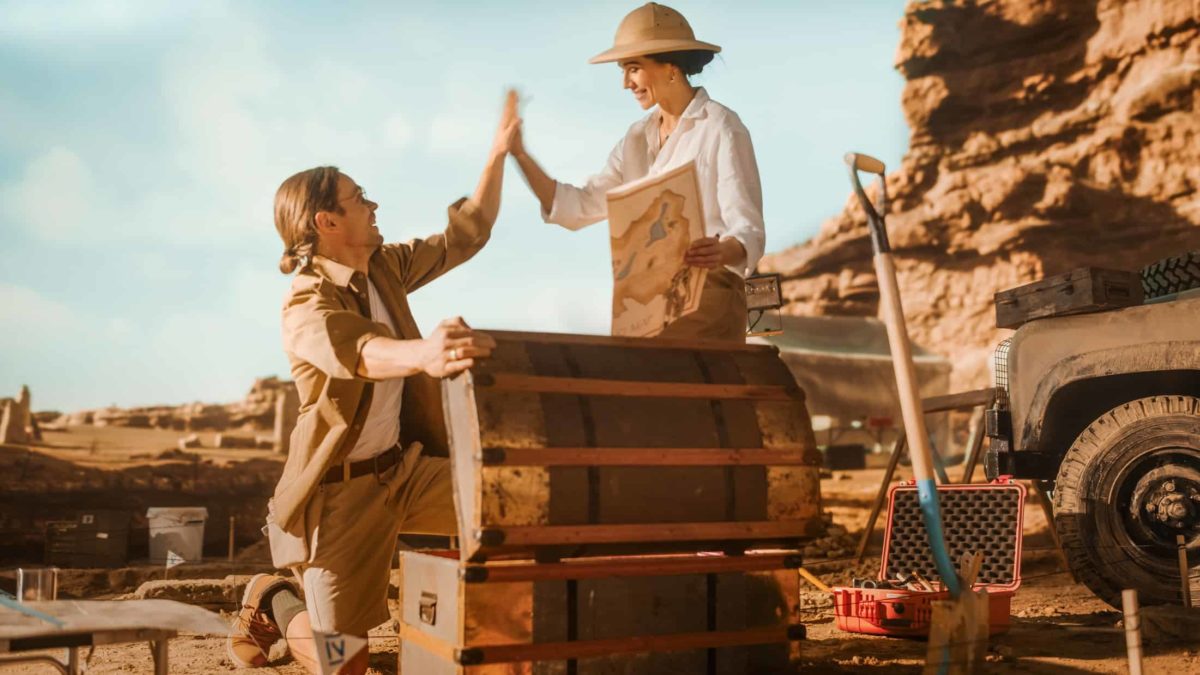 Two treasure hunters high-five after finding a treasure chest buried in the ground