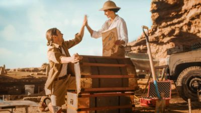Two treasure hunters high-five after finding a treasure chest buried in the ground