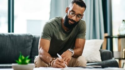 A young man wearing glasses writes down his stock picks in his living room.