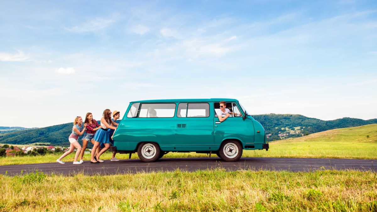 A group of friends push their van up the road on an Australian road.