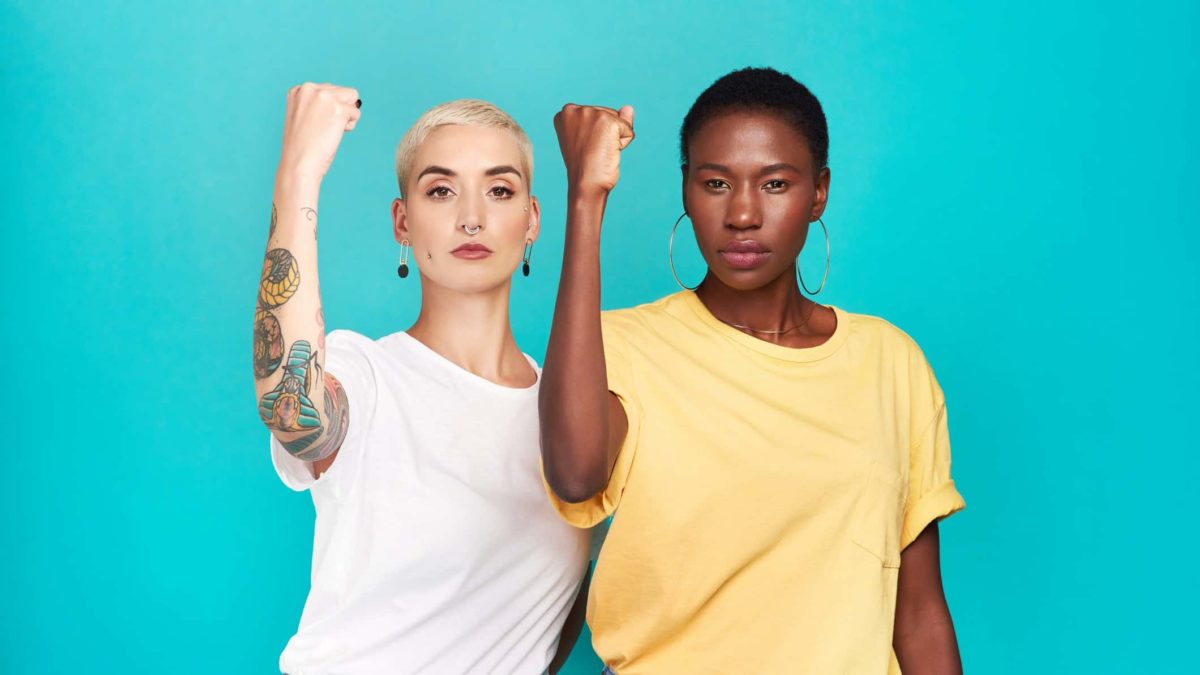 Two women hold up their biceps in a show of strength.