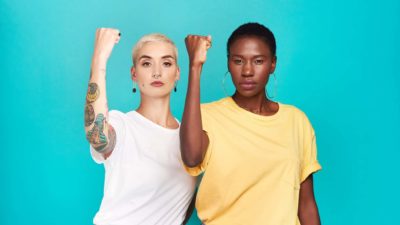 Two women hold up their biceps in a show of strength.