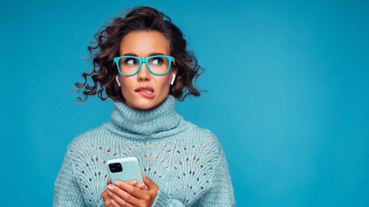 A woman wearing glasses has an uncertain look on her face as she bites her lip, she's just read some news on her phone.