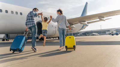 A family walks along the tarmac towards a plane representing more people travelling as ASX travel shares recover