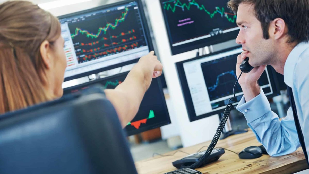 Two brokers analysing the share price with the woman pointing at the screen and man talking on a phone.
