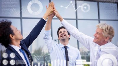 three businessmen high five each other outside an office building with graphic images of graphs and metrics superimposed on the shot.