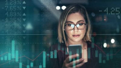 Woman looking at a phone with stock market bars in the background.