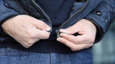 a man's hands hold the ends of the zipper at the bottom of a jacket as if to try to put them together again.