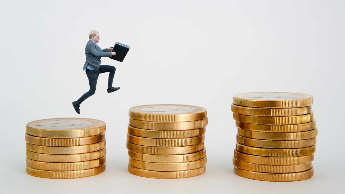 A man leaps from a stack of gold coins to the next, each one higher than the last.