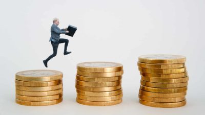 A man leaps from a stack of gold coins to the next, each one higher than the last.