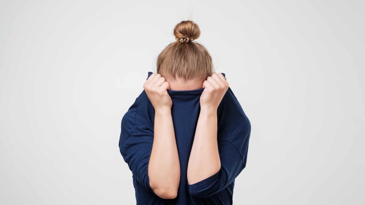 A woman pulls her jumper up over her face, hiding.