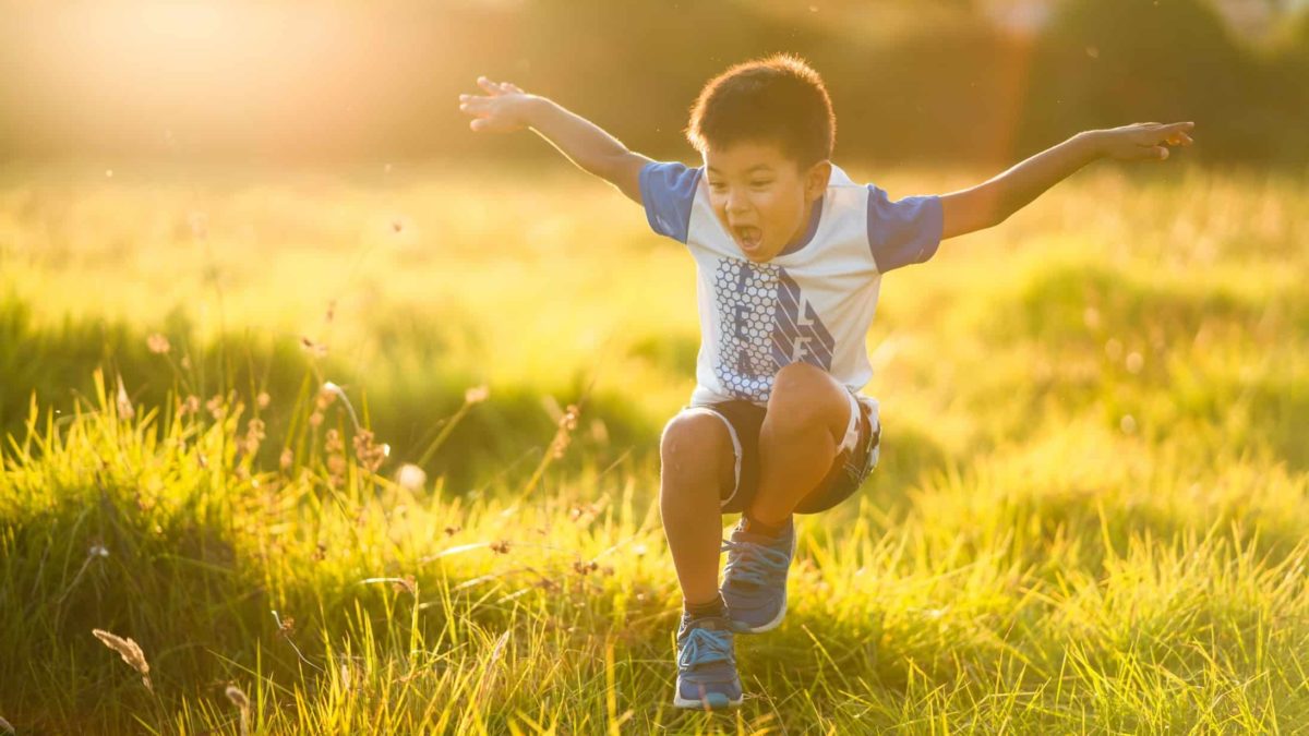 A little boy takes a flying leap over a ditch.