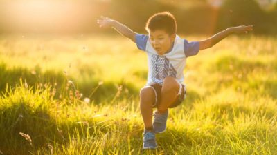 A little boy takes a flying leap over a ditch.