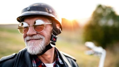 An older man wearing a helmet is set to ride his motorbike into the sunset, making the most of his retirement.