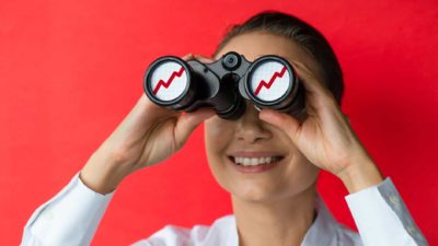A woman smiles at the outlook she sees through binoculars.