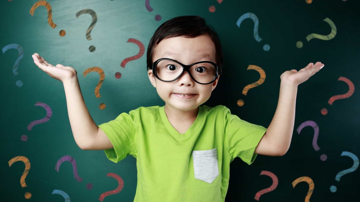 A boy in a green shirt holds up his hands in front of a screen full of question marks.