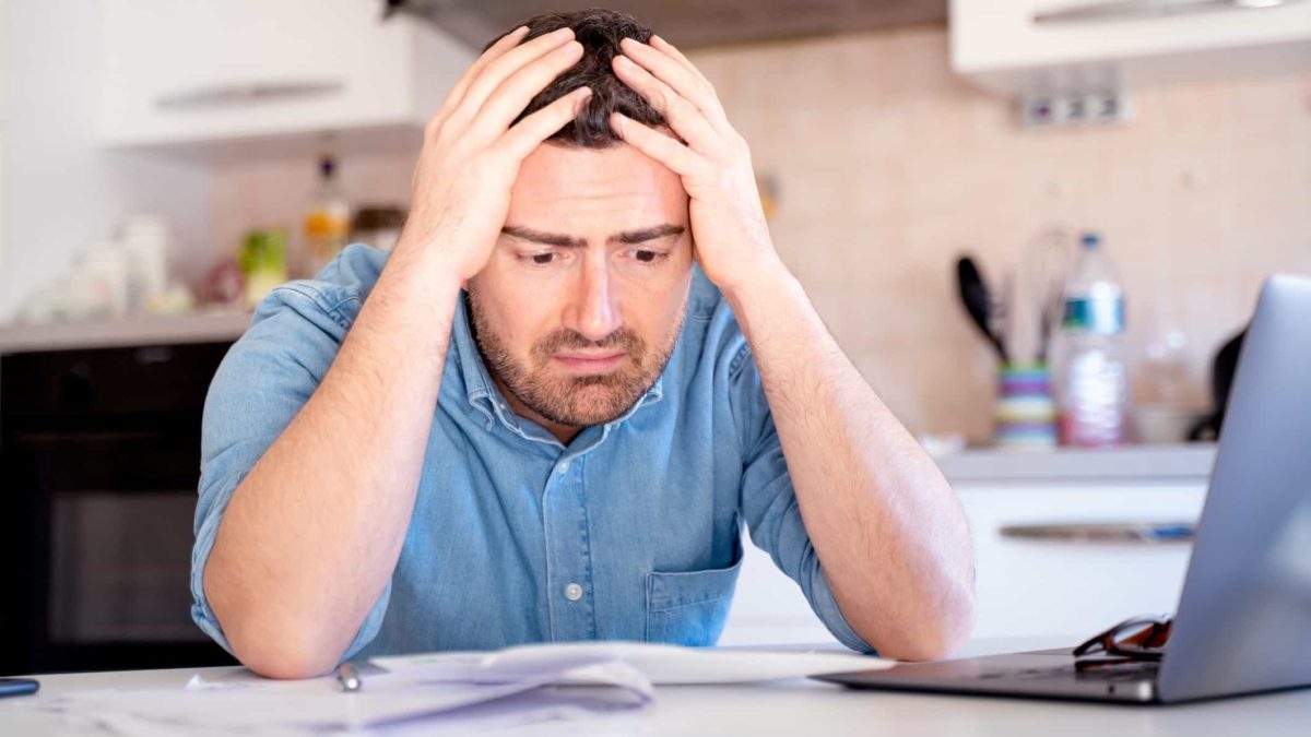 A worried man holds his head and look at his computer.