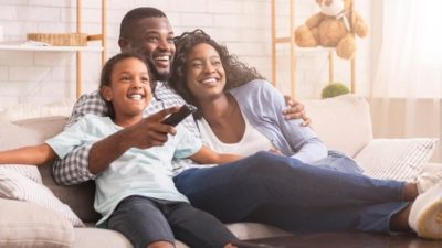 A family of three sit on the sofa while watching television.