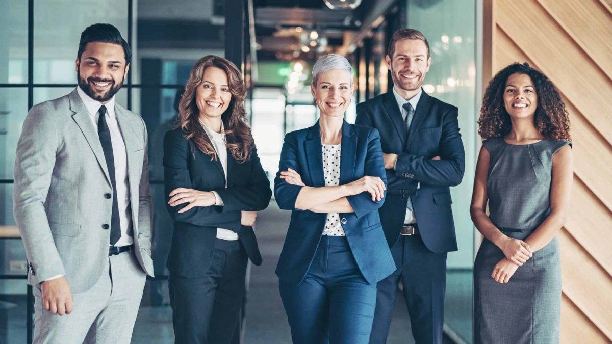 A happy team of businesspeople stand in a corporate office.