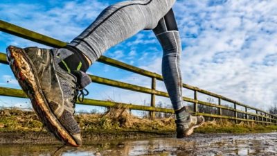 A person runs through the mud alongside a gate.